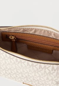 Beige stofpose med diskret MK-logo mønster, gyldent lynlås og indvendig lynlåslomme. Foret med et glat beige materiale med logo print.