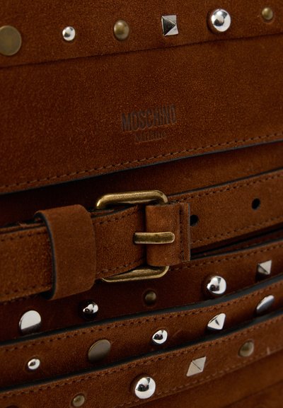 Καφέ σουέντ ζώνη με ορειχάλκινη αγκράφα, διακοσμημένη με ασημένια και μπρούτζινα καρφιά, με ανάγλυφη επωνυμία Moschino Milano.