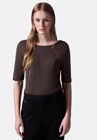 Top marrón de manga corta con cuello redondo, hecho de una tela suave. Combinado con pantalones negros, que muestran un ajuste a medida.