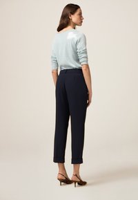  Lichtblauwe pailletten sweater, marineblauwe op maat gemaakte broek en leopardprint hakken. De outfit heeft een relaxed fit en opgerolde broekspijpen.