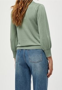 Maglione a maglia verde chiaro con maniche a sbuffo e orlo a coste, abbinato a jeans azzurri a vita alta con tasche posteriori.