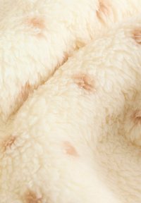 Krämfärgad texturerad tyg har en fluffig yta med mjuka, upphöjda fibrer och sporadiska ljusbruna fläckar.