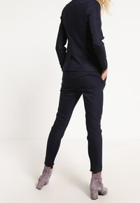 Marinblå skräddarsydd kostym med slim fit byxor och en figursydd kavaj. Kavajen har en en-knappsstängning och är tillverkad av ett mjukt tyg.