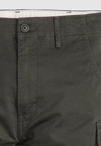 Dunkelgrüne Baumwollhose mit Knopfverschluss, standardmäßiger Taschenanordnung und sichtbarem Nähtextur. Glattes Gewebe mit leichtem Glanz.