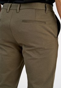 Olijfgroene broek van gestructureerde stof, met een aansluitende snit, riemlussen en twee achterzakken. Eenvoudig, strak ontwerp.