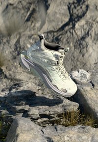Light gray hiking shoe with a textured upper, padded collar, and reflective accents. Features a sturdy sole with aggressive tread.