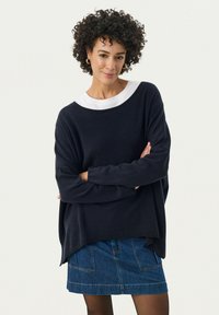 Maglione oversize blu navy con colletto ribbed bianco, morbido al tatto, maniche a pipistrello, abbinato a una gonna di jeans. Stile casual, vestibilità rilassata.