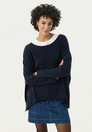 Navy oversized sweater with a white ribbed collar, soft texture, batwing sleeves, paired with a denim skirt. Casual, relaxed fit.