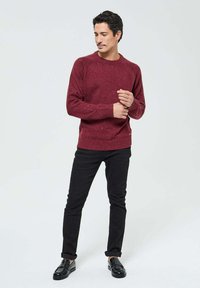 Pull en tricot bordeaux avec un col rond, comportant de petites éclaboussures, des poignets et un ourlet côtelés, porté avec un jean slim noir et des chaussures noires.