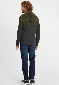 Gebreide hoodie in olijfgroen en donkergrijs, met een gestructureerd ontwerp en ribbels aan de manchetten, gecombineerd met donkere spijkerbroeken en sneakers.