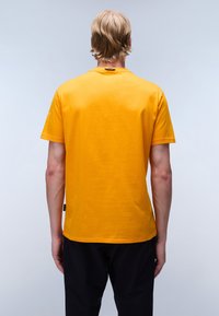 Camiseta de algodón amarilla de manga corta con cuello redondo y dobladillo recto, que presenta un pequeño logo en la parte trasera del cuello.