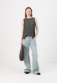 Grå plissert tanktop kombinert med lyseblå vide jeans, holder en brun veske, med svarte sko og en minimalistisk bakgrunn.