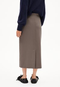 Jupe midi marron clair avec un détail fendu, réalisée en tissu lisse. Assortie à des chaussures noires avec des accents à franges et des garnitures dorées.