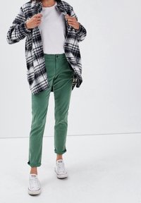 Černobílá kostkovaná košile s bundou, zelené manšestrové kalhoty, bílé tenisky. Bunda má zapínání na knoflíky, kalhoty jsou slim-fit s ohrnutými manžetami.