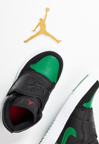 Baskets de sport noires et vertes avec une boîte à orteils perforée, logo en relief et semelle blanche. Accents rouges sur la languette et le logo Jumpman.