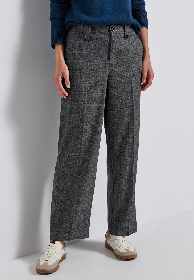 Pantalons à carreaux gris avec une coupe décontractée, dotés de deux poches avant, de fermetures à bouton et d'un tissu texturé. Associés à des baskets blanches.
