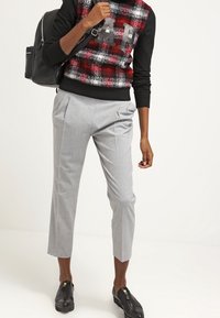 Szare spodnie o prostym kroju, z plisami i gładką teksturą. W połączeniu z czarnym i czerwonym swetrem w kratę oraz czarnymi butami.