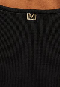 Tessuto nero a coste con un accento in metallo dorato del logo, caratterizzato da una superficie testurizzata e un design senza cuciture nel colletto.