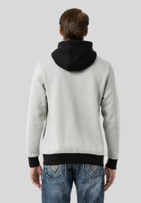 Hellgrauer Sweatshirt mit schwarzer Kapuze, ausgestattet mit gerippten Bündchen und Saum. Die Rückansicht zeigt eine glatte Textur und einen lässigen Schnitt. Getragen mit Jeans.