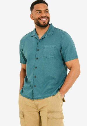 Short-sleeve teal button-up shirt with a chest pocket and classic collar, made from lightweight fabric, paired with khaki cargo shorts.