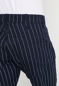 Marinblå byxor med vertikala vita ränder, med en figursydd midja, dubbla bakfickor och mjuk tygtextur.