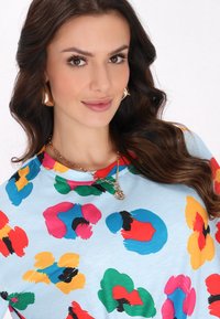 Lyseblå t-shirt med farverige, abstrakte blomster mønstre i rød, grøn, gul og blå. Har rund hals og korte ærmer.