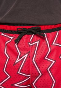 Uppblåsbara idrottsshorts i röd färg med nätstruktur, prydda med zigzag-mönster i vitt och svart, elastisk midja och en svart dragsko.