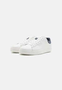Sneaker bianca con tomaia in pelle liscia, chiusura con lacci e accentuazione blu navy sul retro. Suola in gomma testurizzata con un discreto dettaglio del logo.