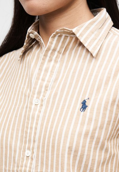 Béžová pruhovaná košeľa s golierom a bielymi vertikálnymi pruhmi. Obsahuje malý modrý vyšívaný motív koňa a gombíkové detaily na légach.