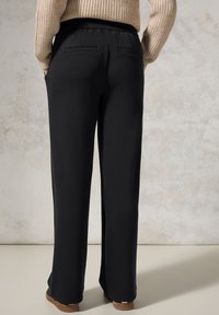 Pantalons noirs à jambes larges avec une taille élastique. Comprend deux poches arrière et une texture lisse et douce. Associés à un pull en tricot beige.