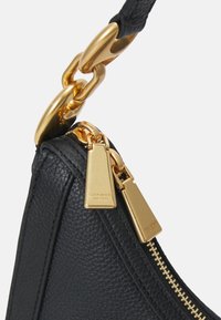 Czarna skórzana torba na ramię z teksturowaną powierzchnią, złotymi elementami, zamknięciem na zamek oraz widoczną metką z logo. Dodatkowym akcentem jest złoty łańcuch.