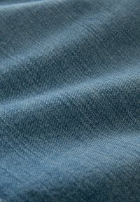 Tela de denim en un azul claro con una textura suave. Presenta un tejido uniforme y sutiles variaciones de color a lo largo de su superficie.