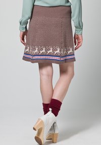 Jupe brune à motifs avec une taille côtelée, ornée de motifs de rennes blancs sur l'ourlet et d'une bande d'accent bleue et rouge.