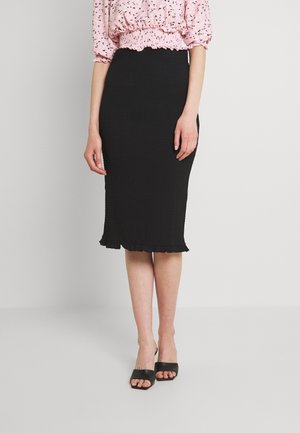 Woman wearing a black knee-length fitted skirt with ruffle hem and black open-toe heeled sandals, paired with a pink patterned blouse.