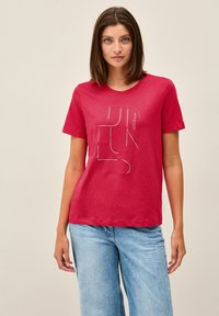 Červené bavlněné tričko s krátkými rukávy a kulatým výstřihem, s bílým geometrickým grafickým designem na přední straně.