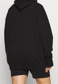 Czarna, oversizeowa bluza z kapturem, długimi rękawami i prążkowanymi mankietami, zestawiona z czarnymi szortami, prezentująca luźny krój.
