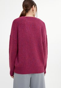 Maglione over-size lavorato a maglia in rosa scuro con sottili striature blu. Presenta un orlo a coste e maniche ampie, evidenziando una finitura testurizzata.