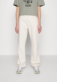 Kermaankermanväriset leveälahkeiset farkut, jotka on valmistettu denimistä. Niissä on etutaskut, nappisuljenta ja rento istuvuus, yhdistetty harmaaseen graafiseen t-paitaan ja lenkkareihin.