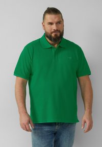 Zielona koszulka polo w jednolitym kolorze, z klasycznym kołnierzykiem i krótkimi rękawami, wykonana z miękkiej, teksturowanej tkaniny. Swobodny krój.