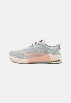 Chaussure de sport Nike gris clair et rose doux avec tige en mesh, semelle amortissante et panneau de soutien translucide au milieu du pied, vue de profil.