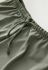 Grüne Sportshorts mit einem gerafften Bund und Kordelzug. Glatte Stoffoberfläche, mit bequemer Passform und ohne sichtbare Muster.