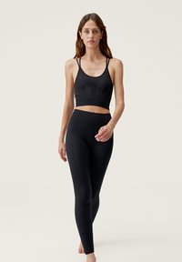Black athletic crop top with thin straps, featuring ribbed texture and seamless design. Paired with high-waisted black leggings, smooth finish.