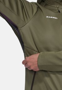 Olivgrüne Zip-Jacke mit glatter Textur, ausgestattet mit einem Logo auf der Brust und einer seitlichen Reißverschlusstasche. Figurbetonter Schnitt mit Kapuze.