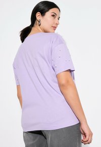 Lavendel kortærmet t-shirt med perleudsmykning på skuldrene, rund hals, afslappet pasform og blødt bomuldsstof.