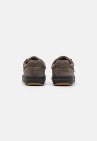 Sivé semišové tenisky majú textúrovaný povrch, plochú čiernu gumovú podrážku a na päte je embosovaný nápis "CONVERSE". Jednoduchý a nízkoprofilový dizajn.