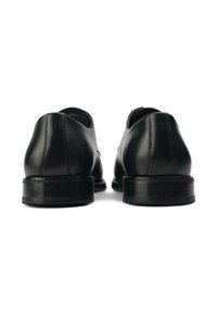 Black leather shoes with a smooth finish, rounded toe, and low block heel. Visible stitching detail at the rear, minimalist design.