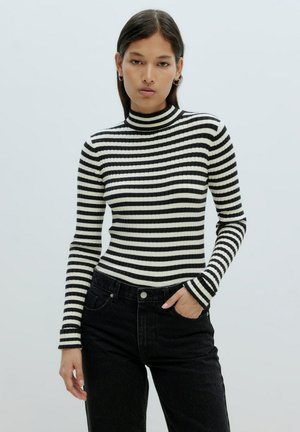 Gestreifter schwarzer und weißer Rollkragenpullover aus geripptem Stoff, taillierter Schnitt mit langen Ärmeln, kombiniert mit hochgeschnittenen schwarzen Jeans.