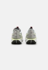 Un par de zapatillas de correr grises y amarillas neón mostradas desde atrás sobre un fondo blanco, con suela negra y tiradores color burdeos.