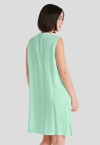Vestido sin mangas de color verde menta en una tela ligera y texturizada, con un patrón sutil y aberturas laterales para facilitar el movimiento.