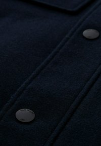 Palton din lână bleumarin, cu nasturi negri cu capse și cusături vizibile, având o suprafață texturată și un design curat, bine structurat.